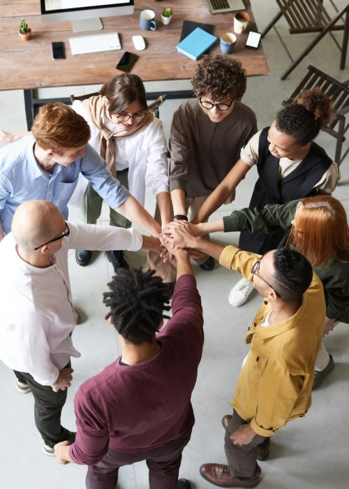 A diverse group of professionals joins hands in a team-building exercise indoors.